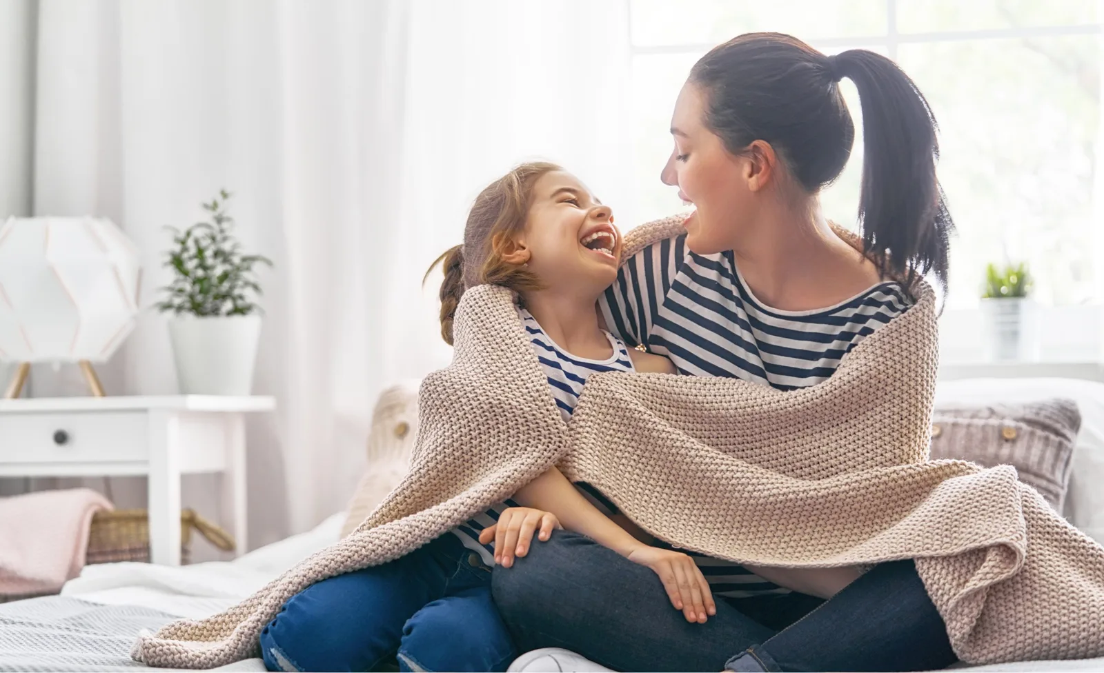 Mother and daughter sitting on bed laughing with each other